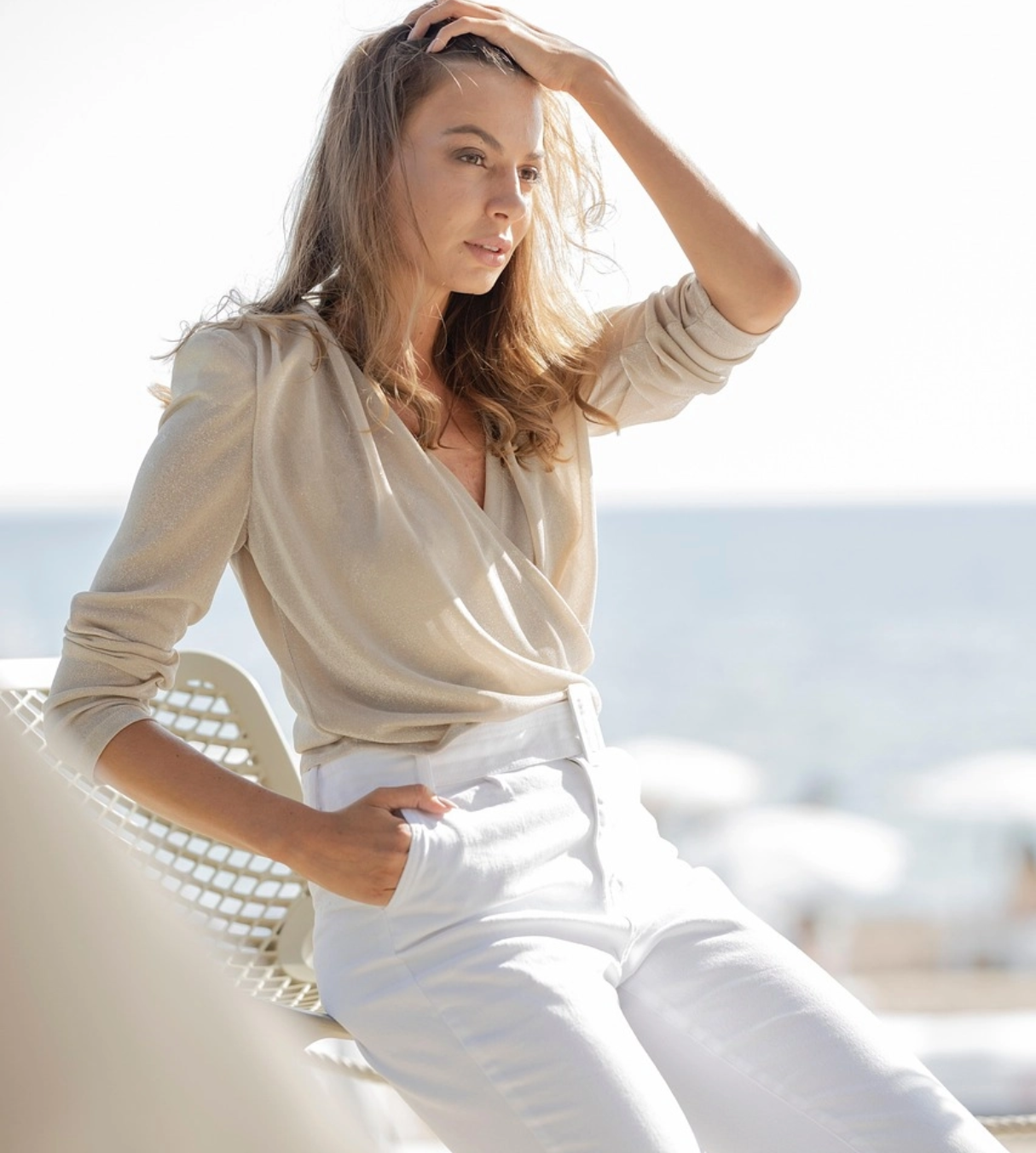 a woman on the beach wearing beige top and white pants